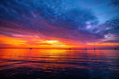 Denizde gün doğumu. Sakin deniz, gün batımında gökyüzü ve bulutların arasında güneş..