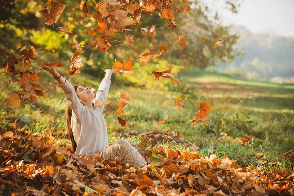 Autumn leaves falling on happy young woman in forest. The colors and mood of autumn. Beautiful young woman throwing leaves in a park. Fall concept. Happy smiling girl with natural red hair.
