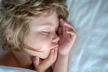 Çocuk uykusu kavramı. Beyaz çarşaflarla rahat bir yatakta uyuyan çocuk..