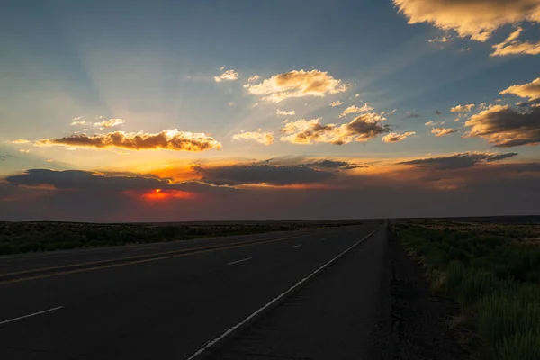 Klasyczny widok panoramiczny na niekończącą się prostą drogę biegnącą przez jałową scenerię południowego zachodu Ameryki. Scena krajobrazowa i wschód słońca nad drogą. — Zdjęcie stockowe