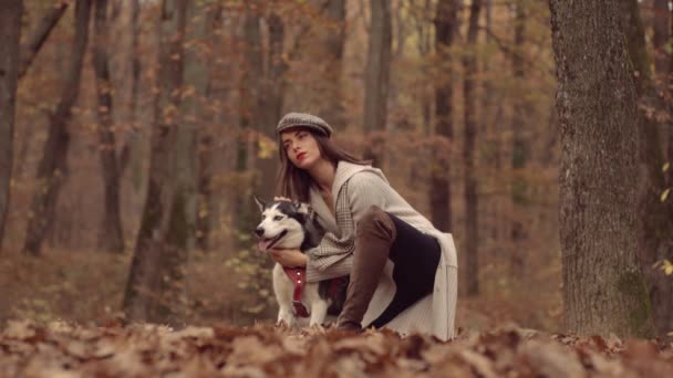 La mujer abraza a su perro mascota. Concepto de moda otoñal. Chica con estilo en estilo otoñal posando sobre fondo de hoja de arce rojo al aire libre. — Vídeos de Stock