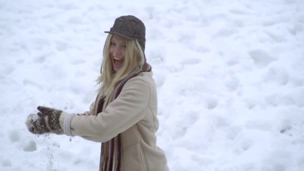 Зимняя девушка бросает снежок в камеру, улыбаясь счастливо веселясь на открытом воздухе в снежный зимний день, играя в снегу. Милая игривая молодая женщина на открытом воздухе наслаждается первым снегом и бросает снежок. — стоковое видео