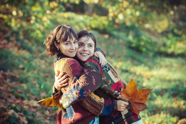 Chica abrazando a su mejor amiga. Dos hermosas amigas en el parque de otoño. Hermosas chicas jóvenes con un ramo de hojas amarillas en sus manos en el parque de otoño. — Foto de Stock