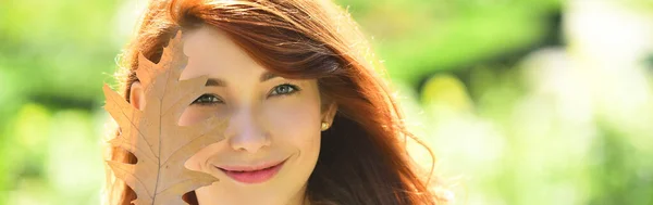 Autumn face close up. Woman fashion model with fall maple leaf outdoors.