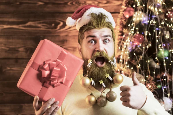 Χριστουγεννιάτικες διακοπές και ευτυχισμένο το νέο έτος. Πορτρέτο του αστείου Αϊ Βασίλη. Ενθουσιασμένος πατέρας με μακριά διακοσμημένη γενειάδα κρατώντας δώρο. — Φωτογραφία Αρχείου