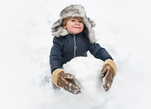 Nettes Kind mit roter Nase und Wintermütze. Fröhliches Kind, das Spaß hat und im Winter Park Schneemänner bastelt. Winterbekleidung für Kinder. — Stockfoto