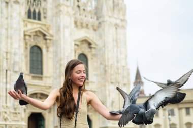 İtalya 'da seyahat eden bir kız. İtalya, Milano 'daki Duomo katedrali yakınlarında poz veren turist kadın. Milan 'daki Piazza Duomo meydanında duran moda kadın turist. Aralarında güvercin oturan komik kız..