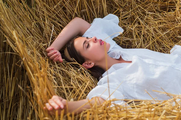 Femme sensuelle couchée dans le foin. Fille en chemise blanche et s'allonge sur une botte de foin. Portrait de femme dans le champ à la campagne. — Photo
