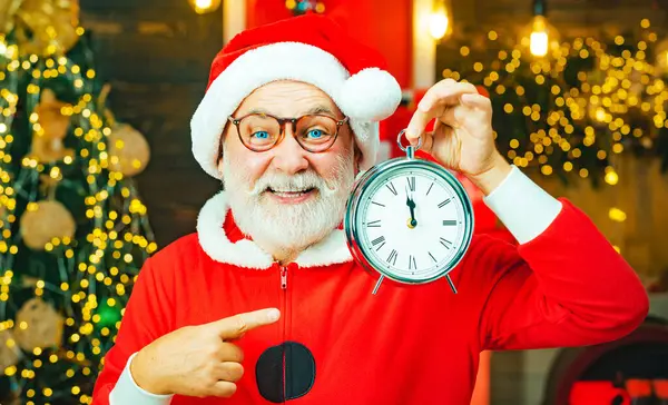 Der Weihnachtsmann macht ein lustiges Gesicht und hält eine Uhr, die fünf Minuten vor Mitternacht zeigt. Weihnachtszeit. Frohe Weihnachten. — Stockfoto