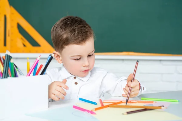 Förvånad söt chil, skriva i anteckningsbok med penna. Skolpojke pojke studerar hemma och gör läxor. — Stockfoto