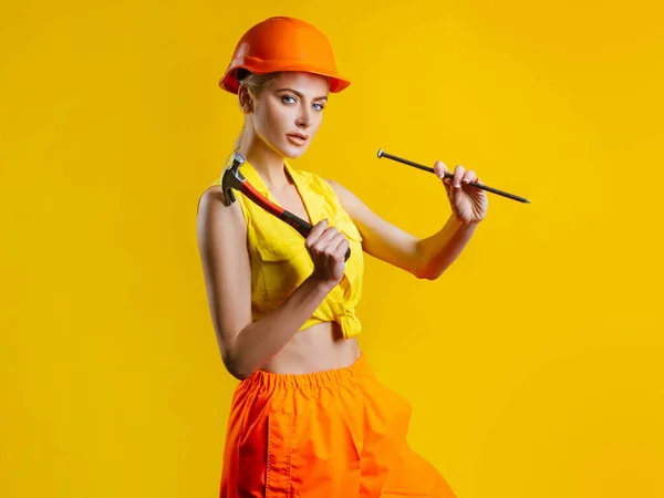 Sarı arka plandaki atölyede çivi çakan genç bir kadın izole edilmiş. Çekiçle inşa edilen kadın modeli. — Stok fotoğraf