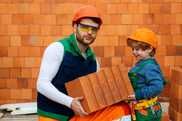 Broeders helpen concept. Bricklayer het installeren van bakstenen op de bouwplaats. bouwer werk met baksteen laag. Broer en kleine jongen werken samen in een werkplaats. — Stockfoto