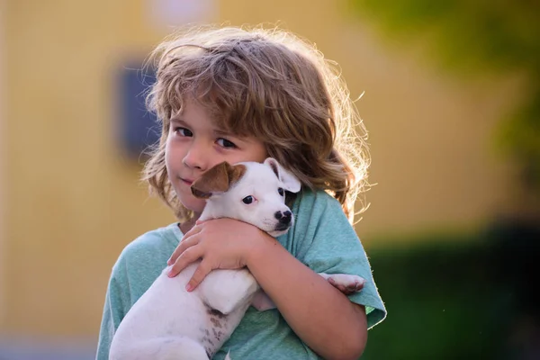 Portrait of kid playing with puppy. Kids and white puppy outdoors in summer. — Stock Photo, Image