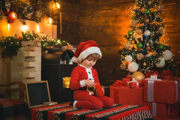 Um miúdo engraçado a segurar um presente de Natal. Criança com dom. Modelos criança se divertindo com o presente. Miúdo a divertir-se perto da árvore de Natal dentro de casa. Crianças de Natal . — Fotografia de Stock