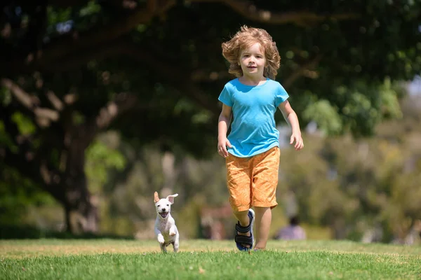 강아지처럼 뛰어. 어린 소년이 애완 동물과 함께 푸른 들판에서 뛰고 있다. — 스톡 사진