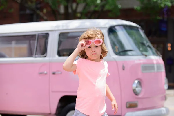 Κομψό μικρό παιδί αγόρι φορώντας ένα καλοκαιρινό ροζ πουκάμισο, αστεία γυαλιά ηλίου διασκεδάζοντας στην πόλη πάνω από πολύχρωμο φόντο. — Φωτογραφία Αρχείου
