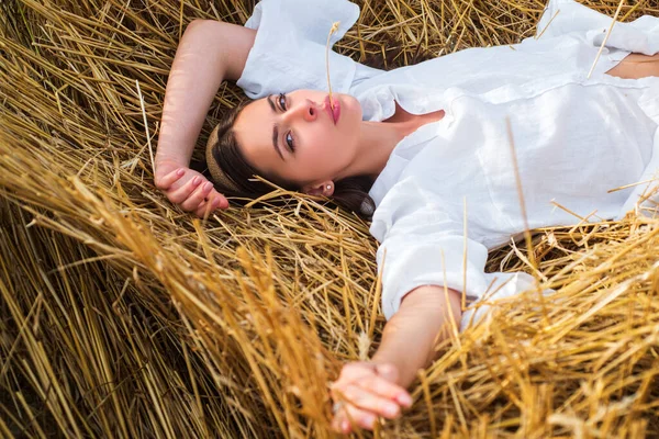 Jeune agricultrice allongée dans un grenier à foin. Sensuelle fille allongée dans le foin, meule de foin. Portrait de femme dans le champ à la campagne. — Photo