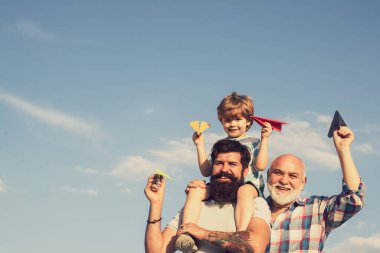 Mutlu bir babanın portresi. Oğlunu sırtında taşıyor ve yukarı bakıyor. Babalar Günü - Büyükbaba, baba ve oğul kucaklaşıyor ve birlikte eğleniyorlar..