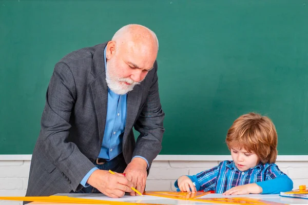 Ученик в классе рисует с учителем. Учитель начальной школы Дедушка оказывает поддержку ученице в классе. Образовательный процесс. — стоковое фото