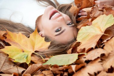 Sonbahar parkında sarı yaprakların üzerine uzanmış güzel bir kız..