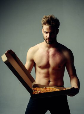 Gri arka planda izole edilmiş İtalyan usulü lezzetli bir pizzayı tutan güçlü, vahşi, sakallı bir adam. Çıplak kaslı gövdeli seksi pizza servisi. Yemek fetişi olan yakışıklı, aç bir adam..