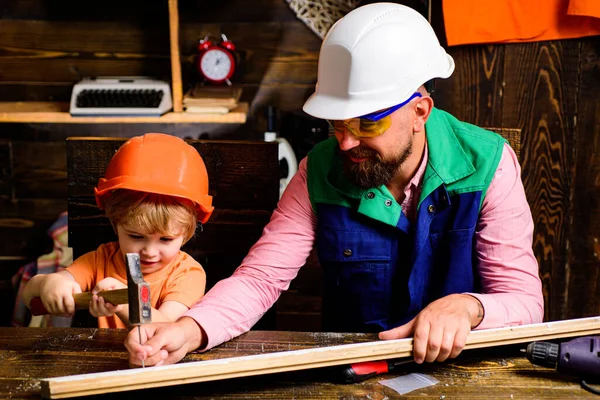 Papa laat zijn zoon zien hoe je diy maakt in een houten werkplaats met hamer en spijker. Vader en zoon gebruiken timmermansgereedschap. Kleine bouwer. — Stockfoto