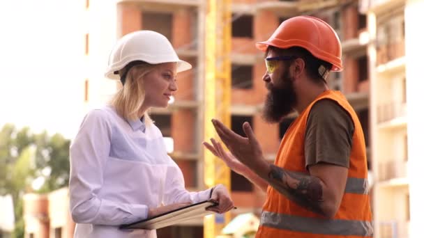 Due ingegneri discutono piano, muro di cemento nel nuovo cantiere. Il capo della costruzione discute i dettagli del lavoro con i lavoratori. — Video Stock