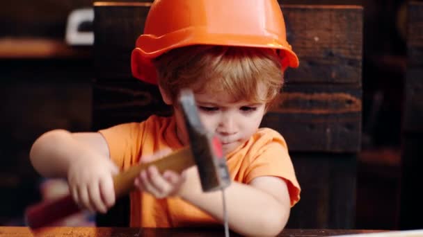 Lustiges Kind im Helm verstopft den Nagel. Cute Kids Baukonzept. Kinder Kreativität Ingenieurausbildung - Junge in der Werkstatt. — Stockvideo
