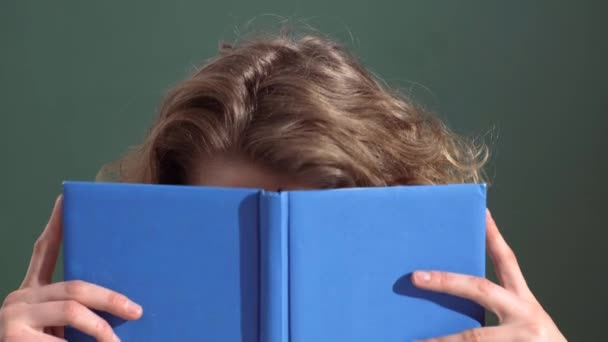 Närbild porträtt av en kvinnlig student. Studentflickan gömmer sig bakom boken. Kvinnan läser en anteckningsbok och täcker sitt ansikte. Inlärning och utbildning. — Stockvideo