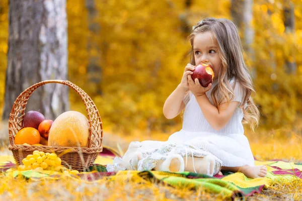 Liten flicka har kul att leka med fallna gyllene löv, äta äpple. Varmt soligt väder. — Stockfoto