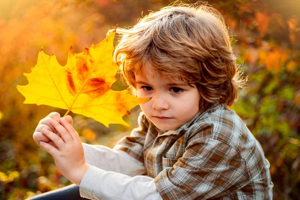 Χαρούμενο παιδί που ονειρεύεται στο πάρκο. Χαριτωμένο αγόρι με φύλλα σφενδάμου έξω. Το παιδί φοράει φθινοπωρινά. Όνειρο παιδιού φθινόπωρο. Πτώση αφήνει τα παιδιά έννοια. — Φωτογραφία Αρχείου