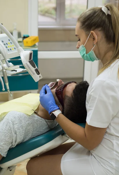 Jovem escolhendo a cor de dentes no dentista, close-up. Homem barbudo a ter dentes examinados em dentistas. Homem sénior a fazer tratamento dentário no consultório de dentistas. Cuidados dentários e clareamento dos dentes. — Fotografia de Stock