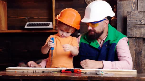 Батько і його маленький син з інструментами в майстерні. Хлопчик-дитина зайнятий в шоломі, навчаючись використовувати молоток з татом. Концепція освіти раннього дитинства . — стокове відео