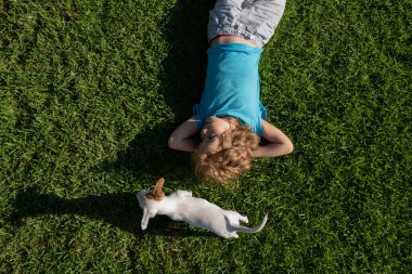 Sevimli çocuk ve yavru köpek çimenlerin üzerinde yatıyor, yaz konsepti, üst manzara.