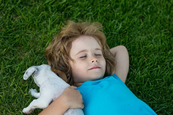 Pequena criança deitada no gramado de um jardim está abraçando cachorro cachorro. — Fotografia de Stock