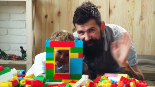 Pai e filho criam construções coloridas com tijolos de brinquedo. Crianças educação infantil. Criança feliz brincando com o pai construção baby sitter construtor de blocos multicoloridos. — Vídeo de Stock