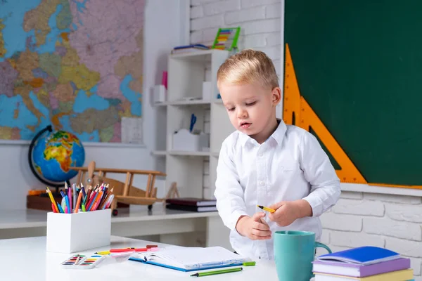 Dzieci szykują się do szkoły. Wnętrza szkoły.Happy cute pracowity dziecko siedzi przy biurku w pomieszczeniach. — Zdjęcie stockowe