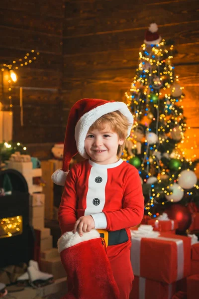 Niedliches kleines Weihnachtsmännchen mit Neujahrsgeschenken auf weihnachtlichem Hintergrund. Weihnachten. Kindheitserinnerungen. Familienurlaub. Weihnachtsmann feiert Weihnachten zu Hause. — Stockfoto