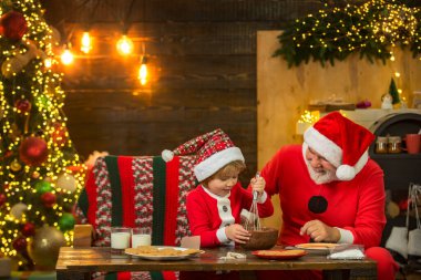 Çocuk Noel Baba zencefilli kek ve sütle eğleniyor. Noel Baba ve oğlu Noel ağacının yanında eğleniyor ve Noel 'i evde kutluyorlar. Komik çocuk Noel kurabiyesi yapıyor..