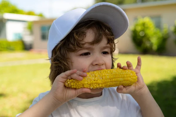 Retrato de um menino bonito comendo milho. Criança no jardim, milho - menino adorável comendo milho na espiga no jardim. Estilo de vida de outono. Comida orgânica caseira. Nutrição de crianças Vegan. — Fotografia de Stock