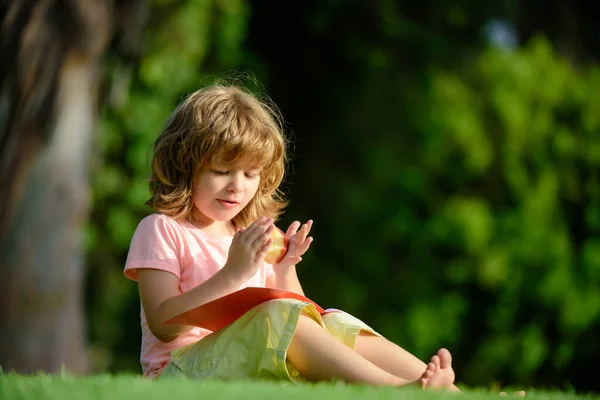 Educación a distancia para niños. Lindo niño estudiando y comiendo manzana afuera en el parque. — Foto de Stock