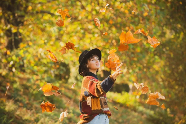 Ragazza modello positivo a riposo. Le foglie autunnali cadono su giovane donna felice in foresta. Concetto di caduta. Donna autunnale nel parco autunnale. Bella giovane donna che lancia foglie in un parco. — Foto Stock