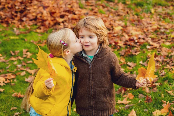 Pequeña pareja linda juguetona niño y niña caminan en el parque de otoño, se divierten, besan, disfrutan de un buen día soleado. —  Fotos de Stock