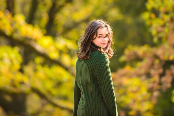 Herbstlicher Teenager-Modetrend. Ein junges Mädchen läuft im Strickpullover durch den Park und hält ein Blatt in der Hand. Außenporträt. — Stockfoto