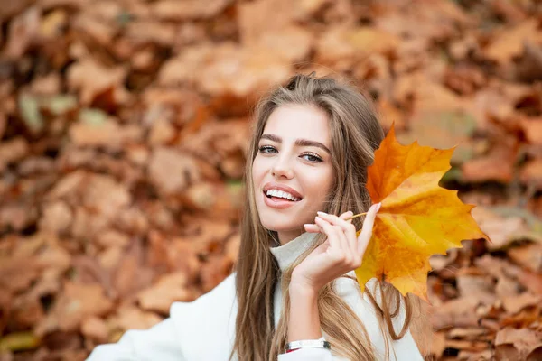 美丽而快乐的女人，面带微笑，手中握着一片秋天的黄叶. — 图库照片