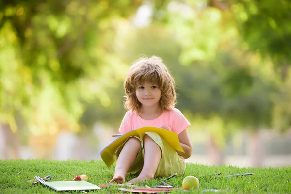 Educação à distância. Bonito sorrindo criança americana estudando e escrevendo com lápis ao ar livre no parque. — Fotografia de Stock