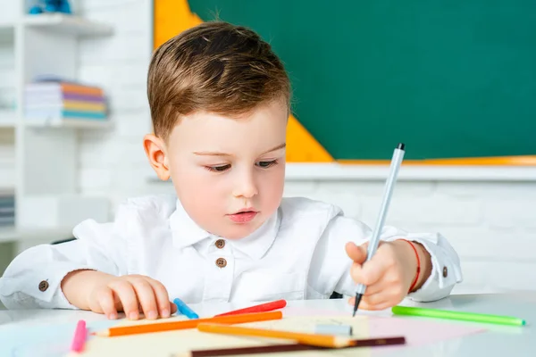 Geconcentreerd schattig kind, schrijven in notitieboekje met behulp van potlood. Schattig kind zit binnen aan een bureau. — Stockfoto
