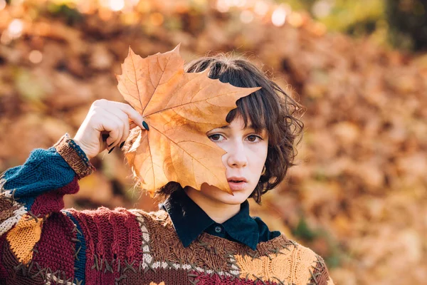 Arka planda düşmüş bir yaprak. Parkta sonbahar kızı. Moda insanları. Sarı akçaağaç yaprağı tutan bir kadın. Sonbaharda genç ve güzel bir kızın portresini çek.. — Stok fotoğraf