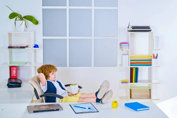 Niño pequeño hombre de negocios usando en formalwear documento de lectura y de pie en la oficina. Empresario Niño en oficina relajándose en silla. Jefe de niños. —  Fotos de Stock