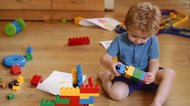 Toddlers build a tower in kindergarten. Child playing with colorful toys. Funny curly baby boy with educational toy blocks. Children play at day care or preschool. Mess in kids room — Stock Video